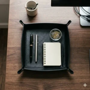 Black leather tray organizing fountain pens, a notepad, and paperclips on a modern office desk.