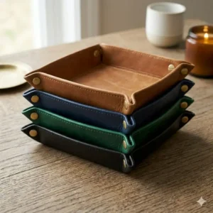 A collection of small leather trays displayed in tan, black, navy blue, and emerald green colors.