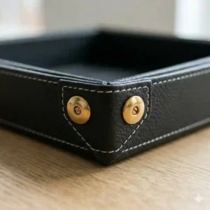 Corner detail of a collapsible black leather valet tray featuring polished brass corner snaps.